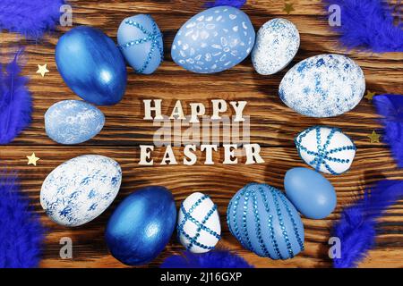 Happy easter, lettering on stylish wooden table, background. Blue and white eggs are everywhere. Colorful Easter eggs, top view. Copyspace. Stock Photo