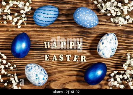 Happy easter, lettering on stylish wooden table, background. Blue and white eggs are everywhere. Colorful Easter eggs, top view. Copyspace. Stock Photo