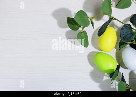 Collecting Easter eggs. Chicken eggs colored green. yellow and white, lie on a white wooden background with branches. Creative greeting card with East Stock Photo