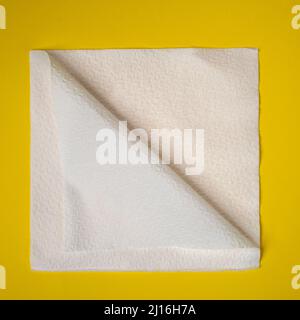 a paper napkin folded diagonally on a yellow surface Stock Photo