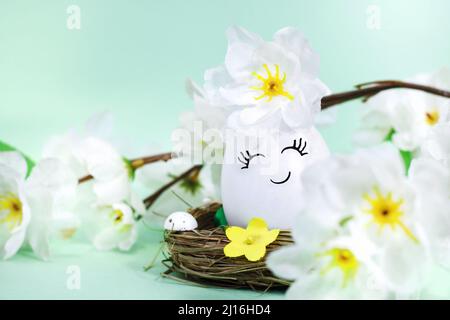 A happy or cute decorated Easter egg in a basket, with flowers on a green background. Easter postcard. Stock Photo