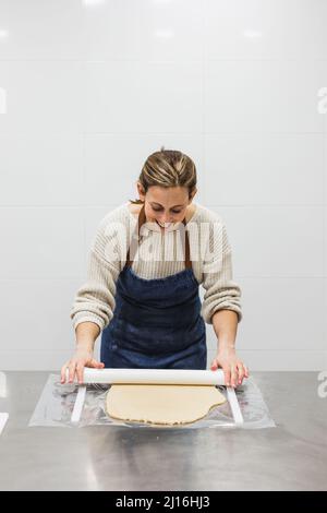 Woman smiling as she kneads dough with kneading stick Stock Photo