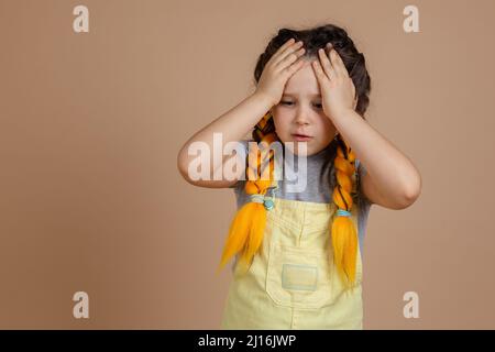 Sad young female with yellow kanekalon braids looking down, with hands put on head thinking about what she has done in yellow jumpsuit and gray t Stock Photo