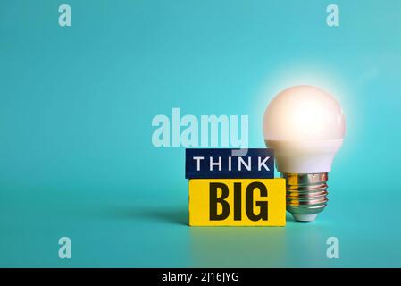 Glowing lightbulb and wooden cube with text THINK BIG on green background. Copy space for text. Stock Photo