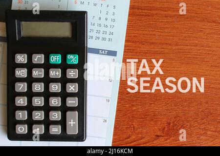 Top view image of calculator, calendar and text TAX SEASON on wooden table. Stock Photo