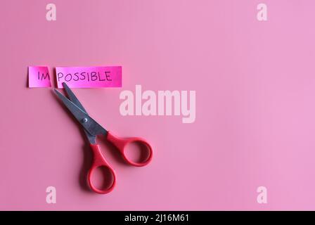 Cutting the word impossible to possible on pink background, concept for self belief, positive attitude and motivation. Stock Photo