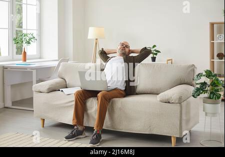 Man takes break while working on laptop computer sitting on couch in his home office Stock Photo