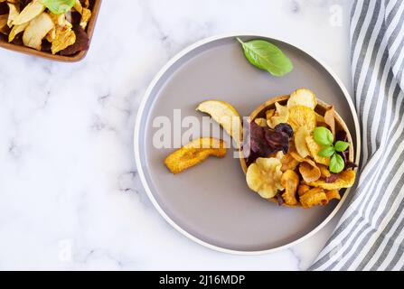 Vegan snacks, multicolored vegetable and fruits chips in wooden bowl , selective focus. Flat lay. Bowl of healthy vegetable chips from beets, sweet po Stock Photo