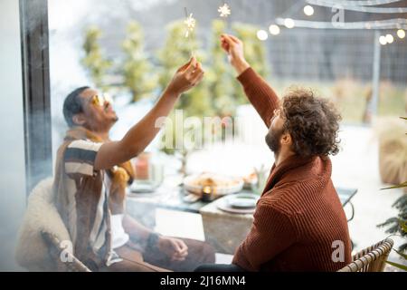 Two male friends celebrating with sparklers at backyard Stock Photo