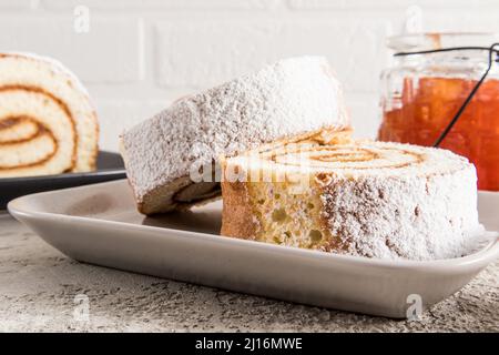 two pieces of tender apple roll on a ceramic plate against a white brick wall and a jar of jam. delicious dessert. Snack Stock Photo