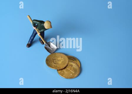 Cryptocurrency bitcoin mining concept. Miniature miner working to get bitcoin. Blue background Stock Photo