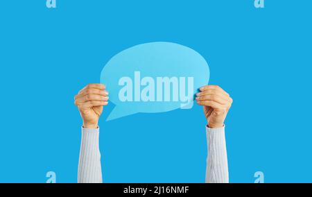 Unrecognizable woman holding empty blue speech bubble in hand on blue background. Stock Photo