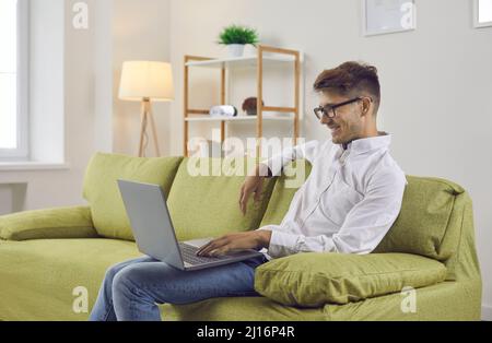 Happy young man watching videos on his laptop computer while sitting on sofa at home Stock Photo