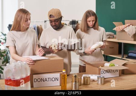 Group of multi-ethnic volunteers working together in charity organization sorting and packing food products for donation Stock Photo