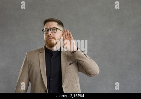 Curious man with a worried expression holds his hand to his ear overhearing a secret conversation. Stock Photo