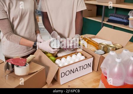 High angle shot of unrecognizable volunteers wearing protective gloves packing food supplies into cardboard boxes for donation Stock Photo
