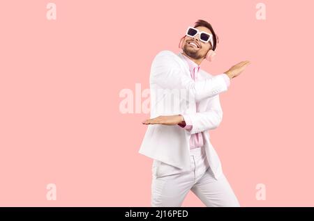Cheerful and joyful carefree young man in stereo headphones dancing happily on pink background. Stock Photo