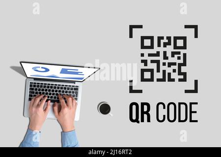 A person is working on a laptop with an image of a QR code icon next to it Stock Photo