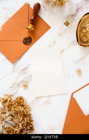 Wedding stationery in autumn style on marble background. Empty paper card mockup, bronze envelopes, dry flowers. Stock Photo