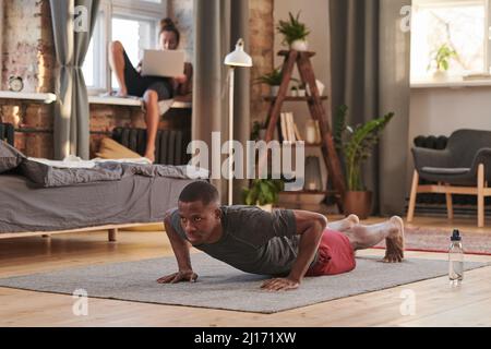 Horizontal shot of handsome young adult African American man doing strengthening push up exercise at home, copy space Stock Photo