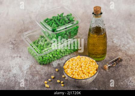 Plastic container with different organic deep frozen vegetables on table. Green peas, sweet corn and cut green beans in a box Stock Photo