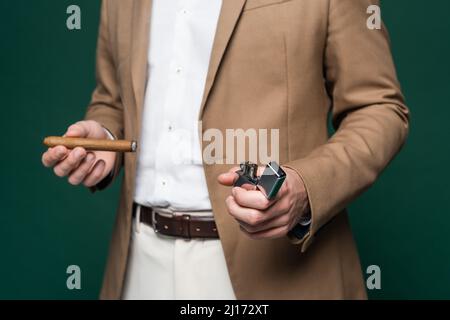 partial view of man in blazer holding cigar and lighter on dark green Stock Photo