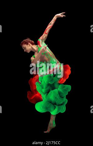 Portrait of young tender woman covered with red and green paint and dye splah dancing isolated over black background Stock Photo