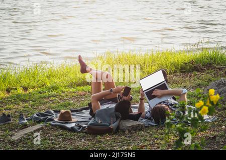 Gay couple couple using laptop and while lying on grass in park. Stock Photo