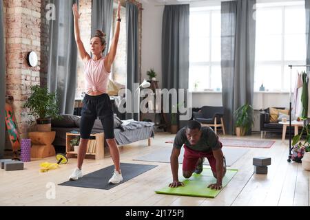Horizontal wide shot of sporty young man and woman exercising in morning in loft living room at home Stock Photo