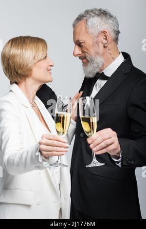 Side view of happy mature woman holding glass of champagne near groom isolated on grey Stock Photo