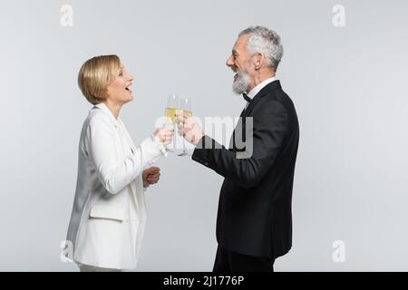 Side view of positive bride clinking champagne with mature groom isolated on grey Stock Photo
