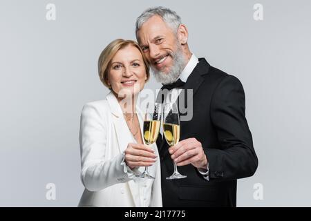 Smiling mature groom looking at camera near bride with champagne isolated on grey Stock Photo