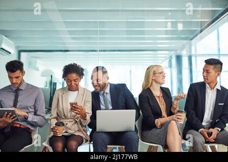 What a friendly environment to work in. Shot of a group of focussed young businesspeople seated together on chairs and making notes using different Stock Photo