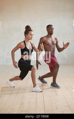 Vertical studio full shot of sporty young Black man and Caucasian woman doing strengthening workout in loft studio room Stock Photo