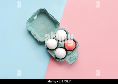 Happy Easter. Top view of chicken eggs and easter painted egg in an open blue cardboard box over pink and blue background Stock Photo