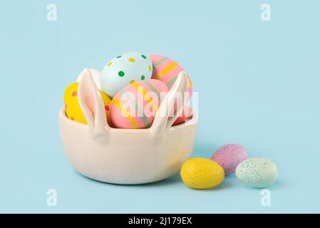 Happy Easter. Colored easter painted eggs in a bunny ears bowl over blue background Stock Photo