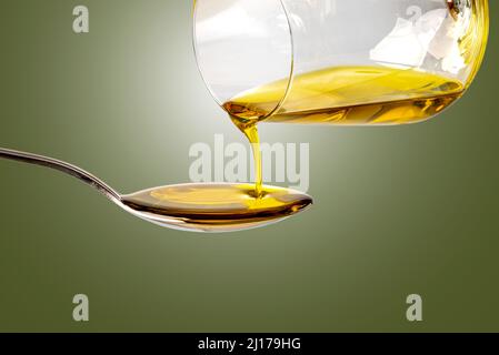 Extra virgin oil poured from glass into spoon, isolated on green background with spotlight, clipping path Stock Photo
