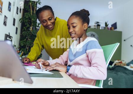 Mother looking at daughter studying on tablet PC in bedroom Stock Photo