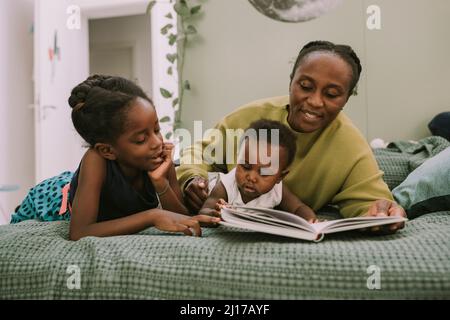 Mother with children reading book lying on bed at home Stock Photo