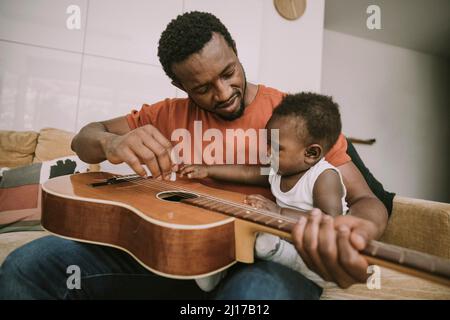 Father showing guitar to baby boy in living room Stock Photo