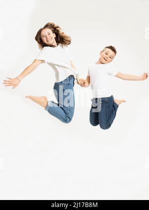 Cheerful brother and sister jumping against white background Stock Photo