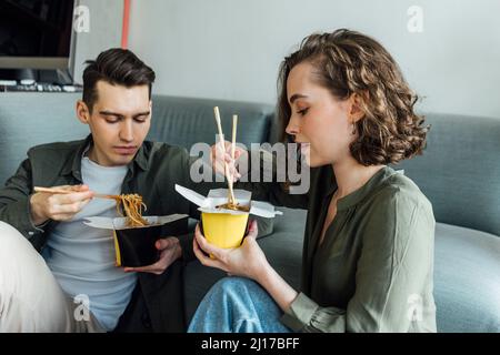 Young couple with chopsticks eating noodles at home Stock Photo