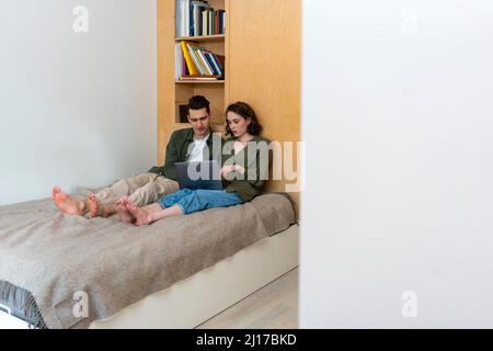 Young couple sharing laptop sitting on bed at home Stock Photo