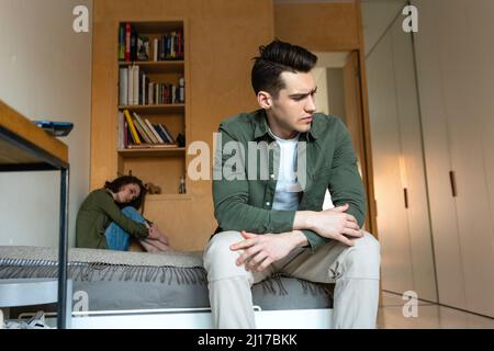 Sad young woman looking at displeased boyfriend sitting on bed at home Stock Photo