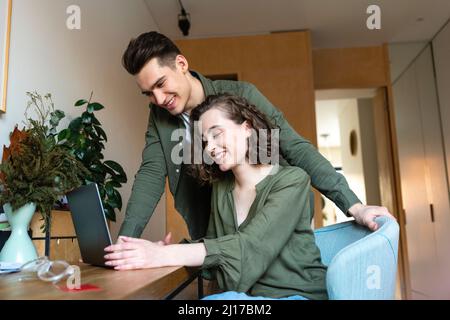 Smiling young man looking at woman using laptop at table Stock Photo