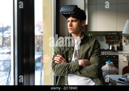 Young man wearing virtual reality simulator standing with arms crossed looking through window Stock Photo
