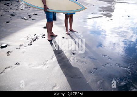 Man with surfboard standing with friend at beach Stock Photo
