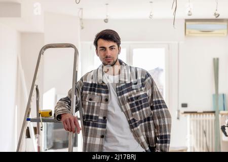 Young man standing by ladder at home Stock Photo