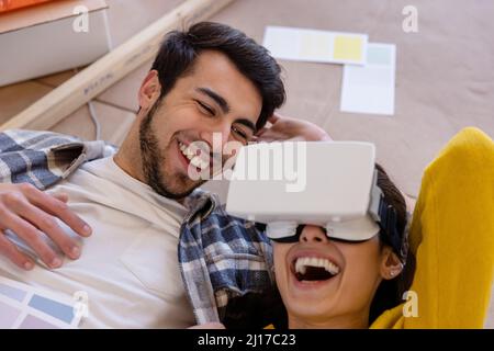 Happy woman with VR glasses lying by boyfriend at home renovation work Stock Photo
