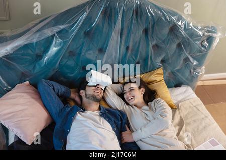 Young man with VR glasses lying on bed by girlfriend in bedroom Stock Photo